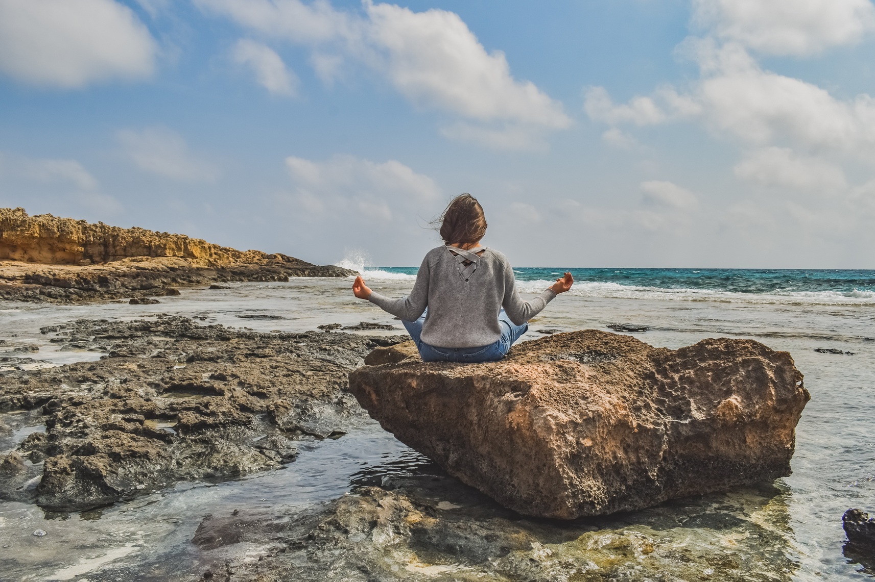Meditation und Ruhe: Frau sitzt entspannt auf einem Felsvorsprung am Meer und atmet achtsam.