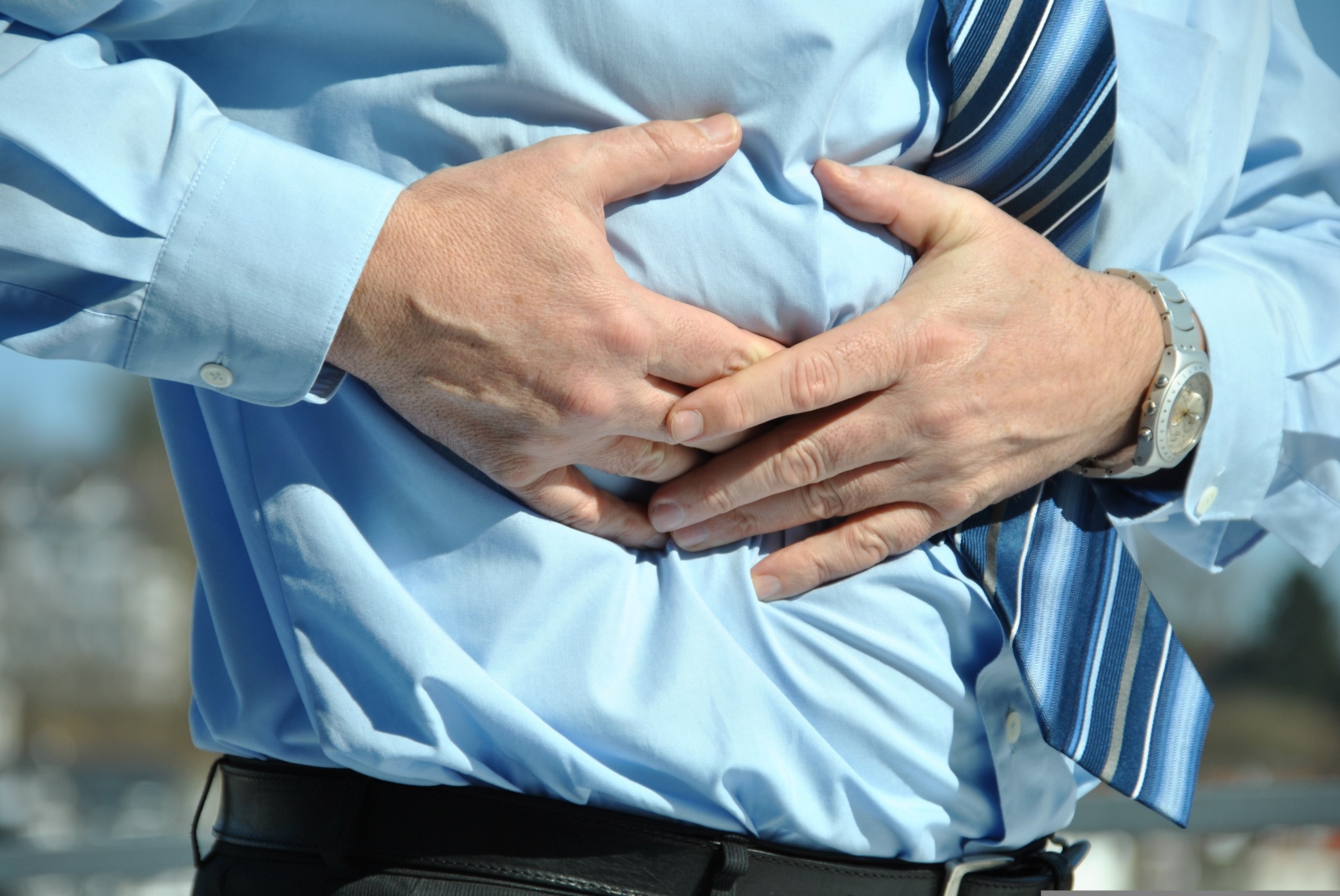 Mann mit Hemd und Krawatte hält sich schmerzgeplagt den Bauch – Hypnose bei chronischen Schmerzen.