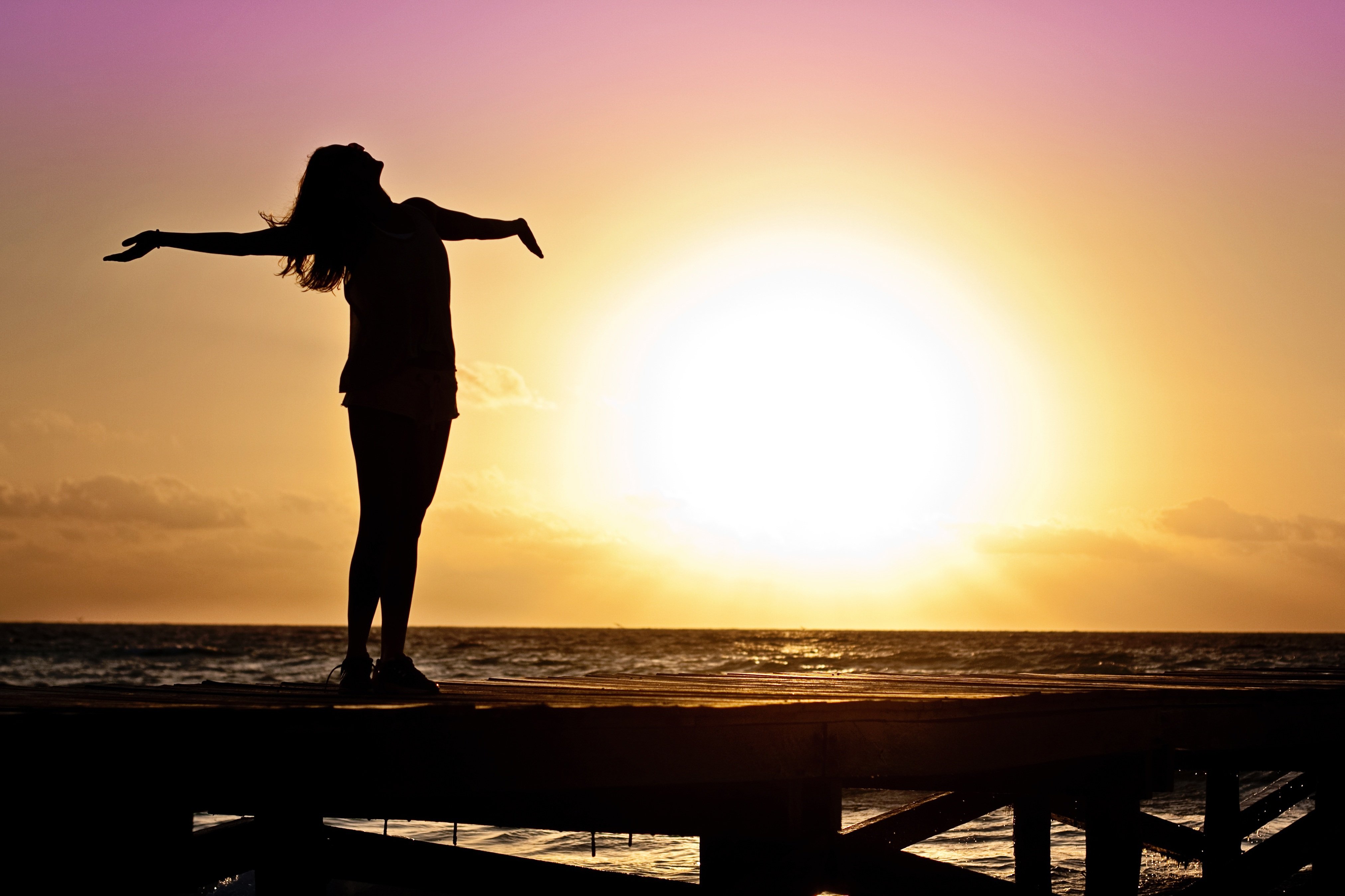 Frau genießt Sonnenuntergang - ausgestreckte Arme als Symbol für Freiheit und Frieden.